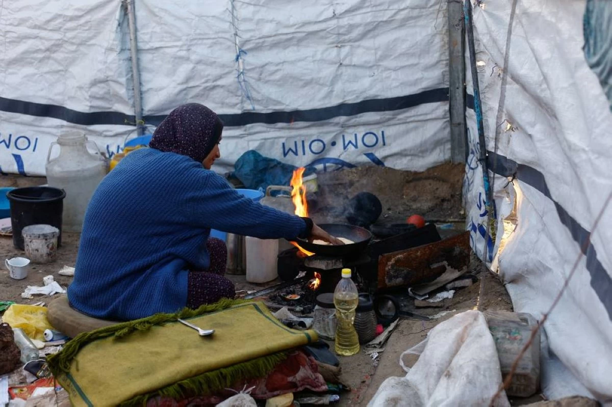 صوره – امرأة فلسطينية نازحة تطبخ على موقد الحطب في خيمة بمدينة دير البلح وسط قطاع غزة. (رويترز)