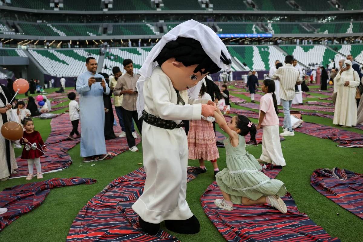 صوره – شخص يرتدي زيًا يلعب مع طفل في استاد المدينة التعليمية حيث أقيمت صلاة عيد الأضحى.